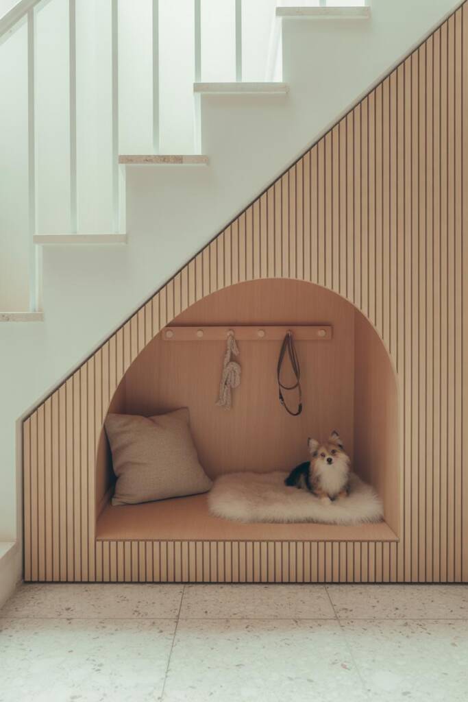 Scandi-style under-stair nook with pale oak slat façade, rounded doorway, interior in warm birch ply, faux-sheepskin pad, neu