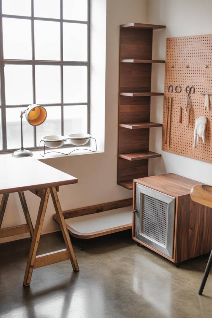 Creative studio with drafting table on sawhorse legs, pegboard tool wall, and concrete floor. A slim black steel-frame pet be